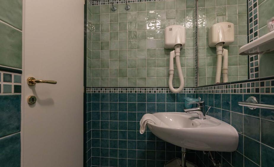 Bathroom with green tiles and wall-mounted hairdryers.