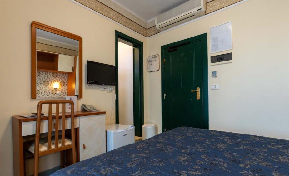 Hotel room with bed, desk, TV, and air conditioning.
